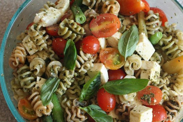 Pesto pasta salad with tomatoes and mozzarella in a glass bowl